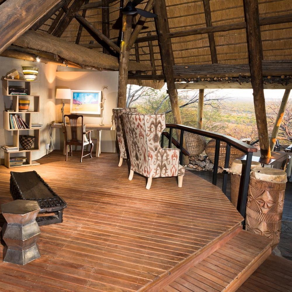 A rustic wooden viewing lounge at Ongava Lodge features patterned armchairs facing an open view of the wilderness.