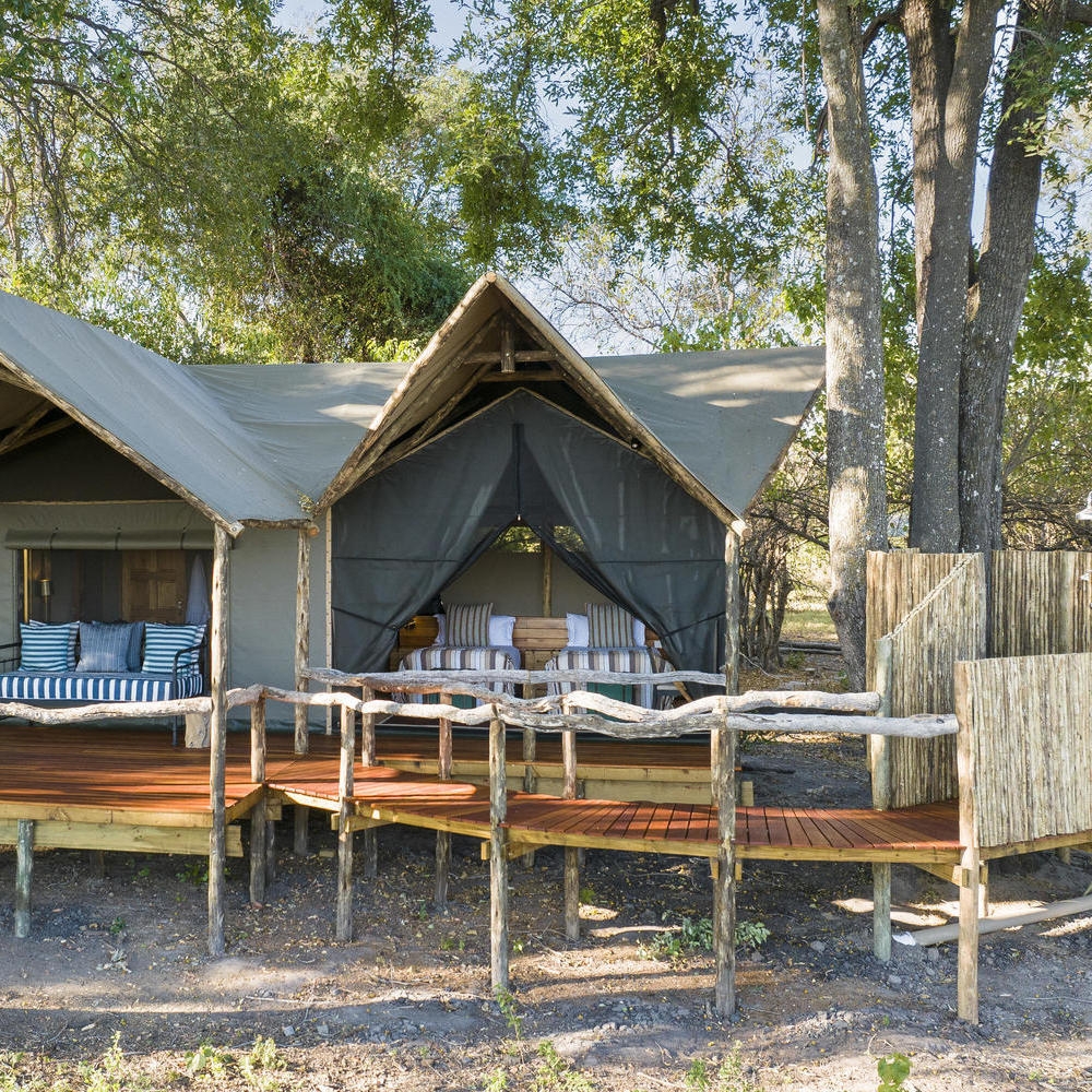 A canvas safari tent with a peaked roof and wooden balcony situated in a wooded area.