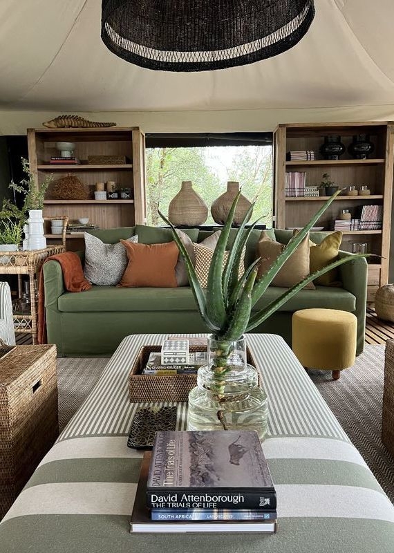 Interior of a luxury safari lounge with a green sofa, striped ottoman, and books at Simbavati Hilltop Lodge.