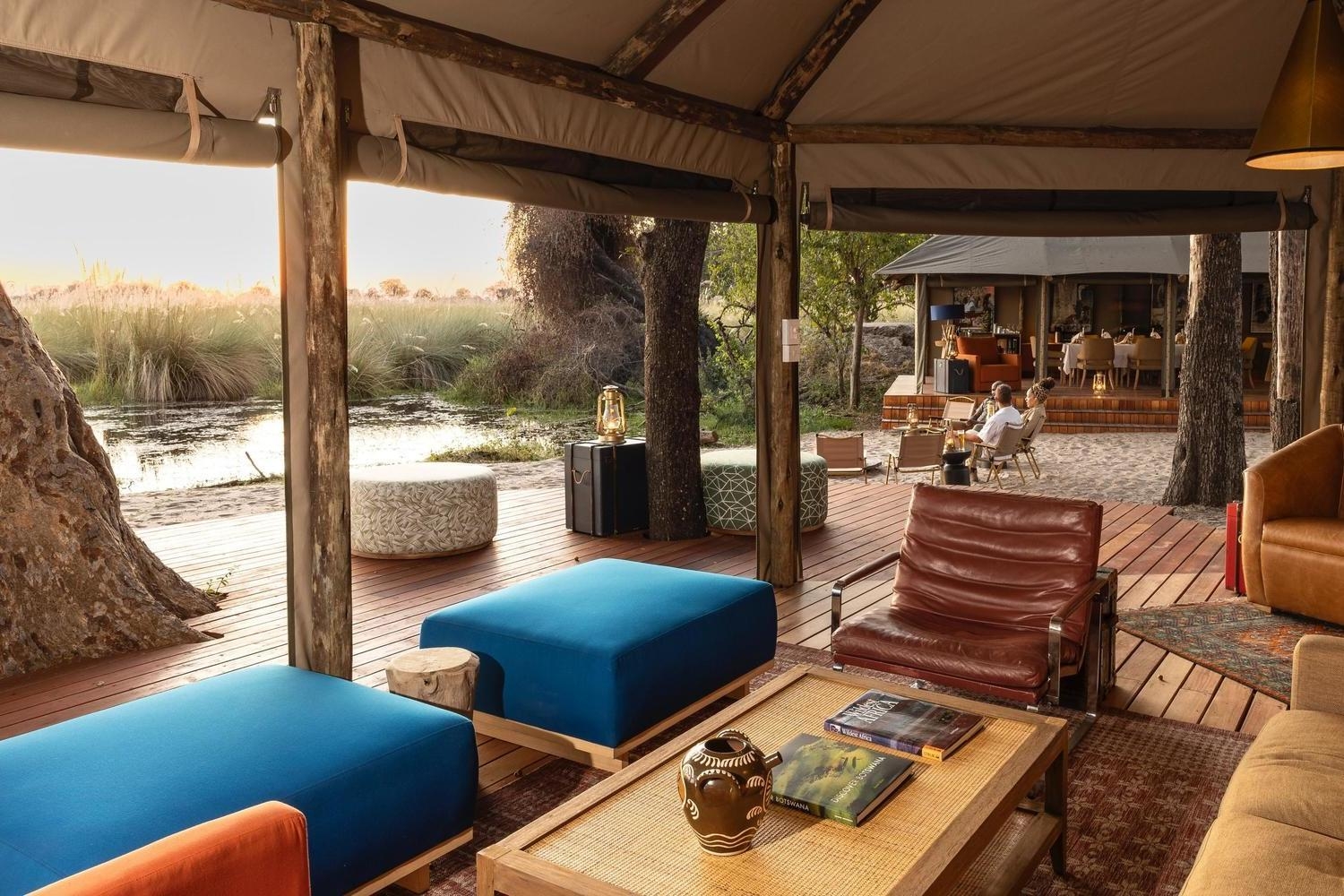 Interior of a luxury safari lodge lounge with blue ottomans and a leather chair overlooking a river.