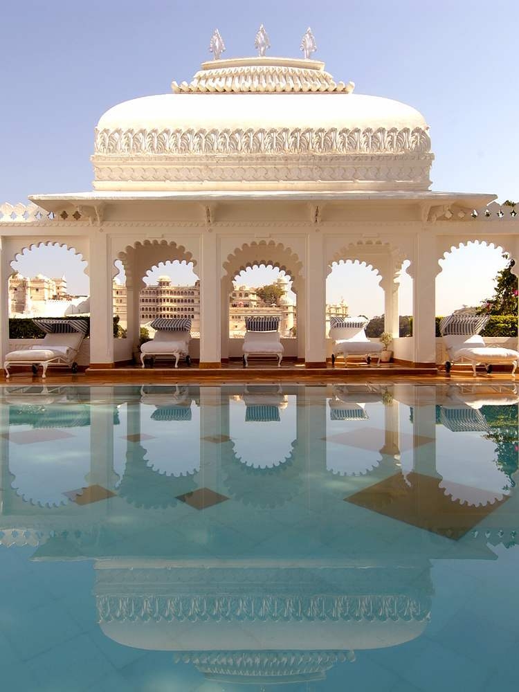 The pool area at Taj Lake Palace featuring sunbeds in between ornate arches.