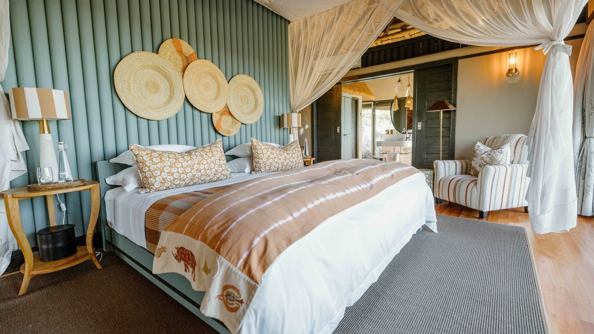 A luxury lodge bedroom with a draped four-poster bed, wooden floors, and a thatched ceiling.