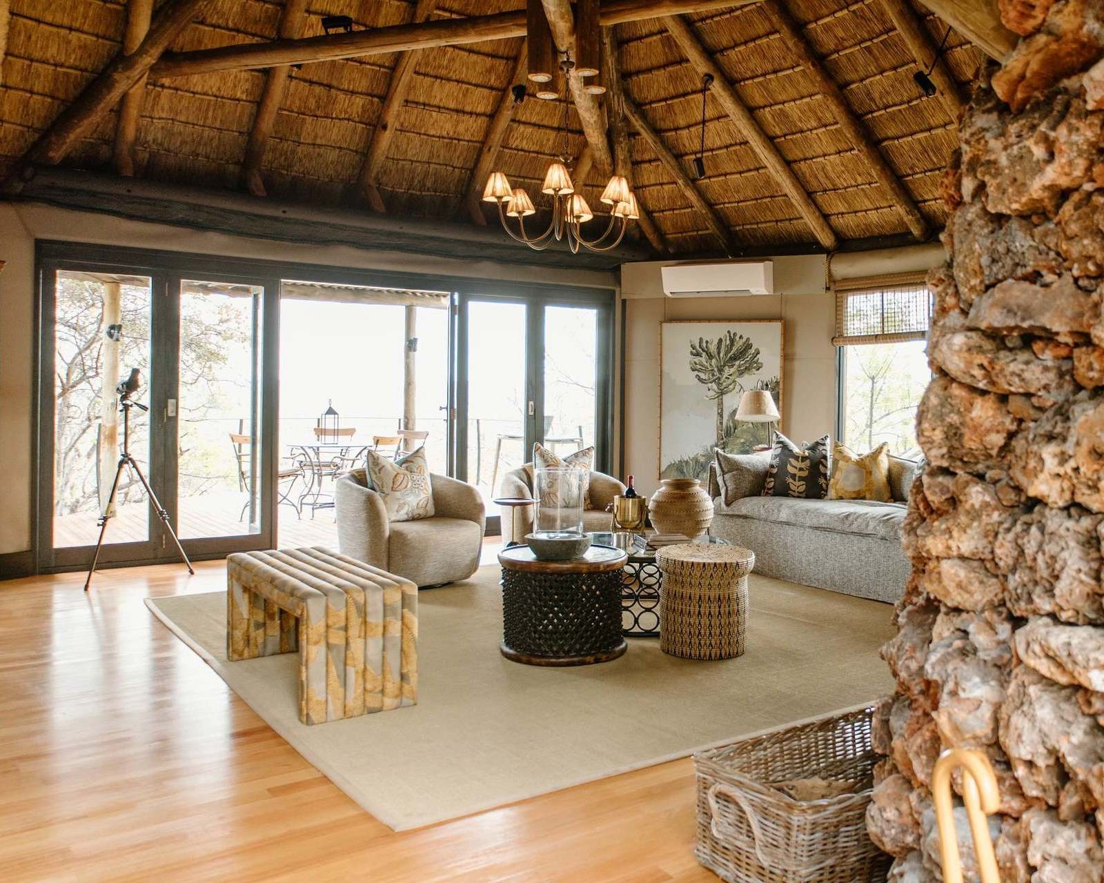 Luxury safari lodge lounge with a thatched roof, comfortable sofas, and large glass doors leading outside.