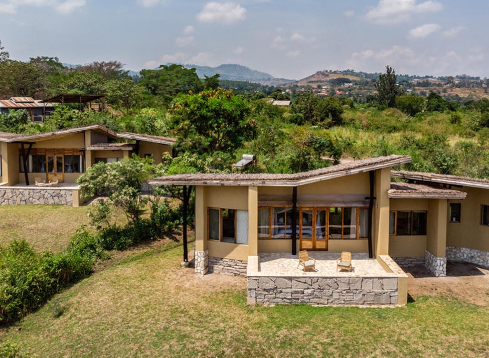 Two earth-toned buildings with stone patios and slanted roofs surrounded by greenery at Kyambura Gorge Lodge.