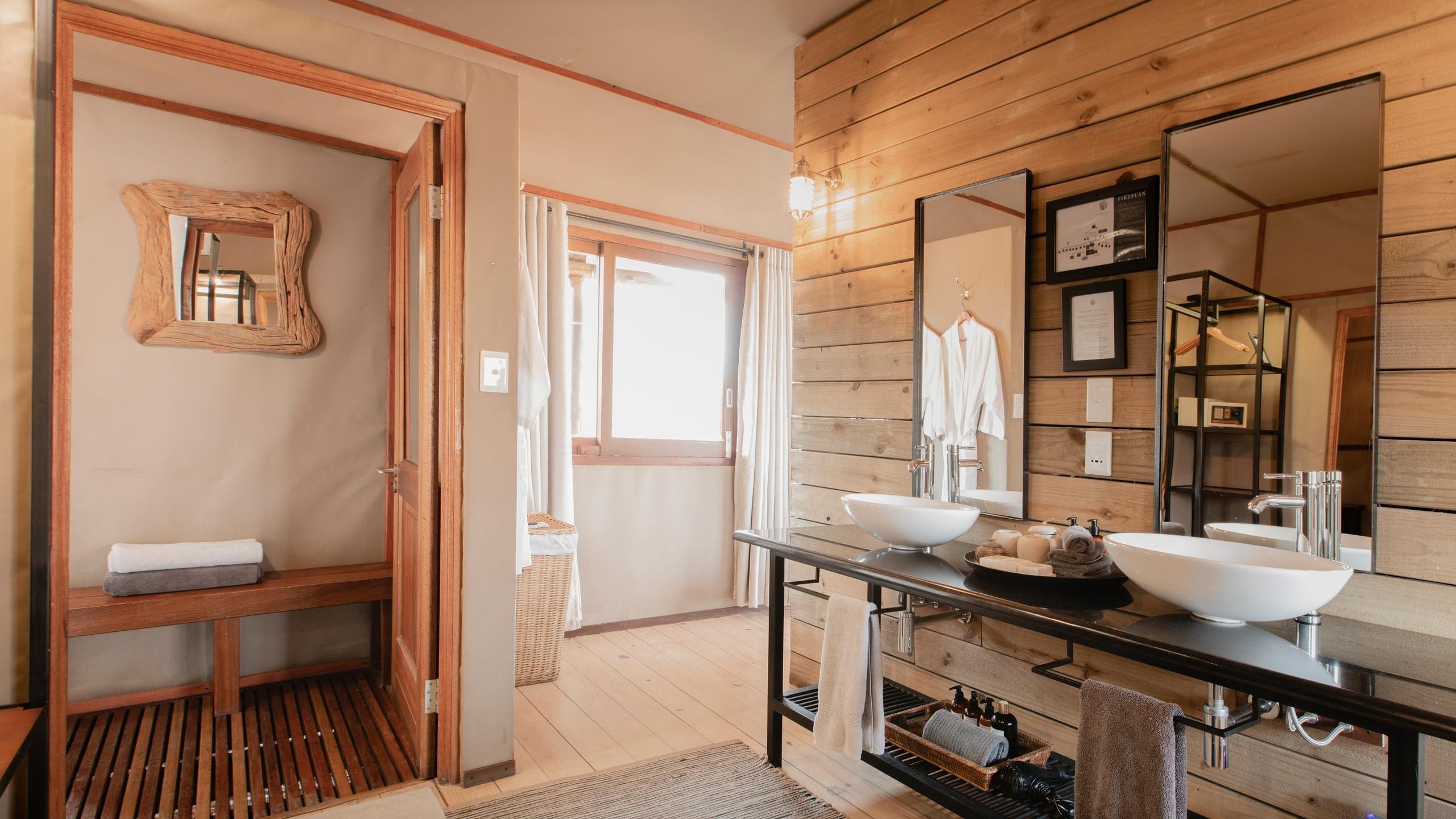 Rustic bathroom interior with a double vanity, white vessel sinks, mirrors, and an open doorway leading to a wooden shower.