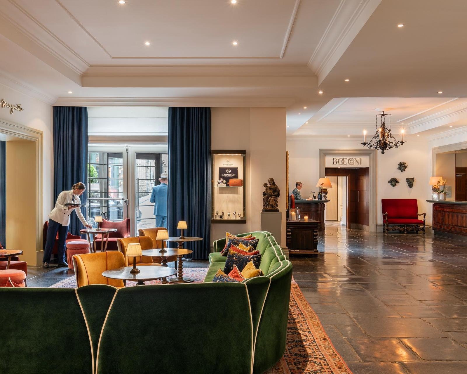 Elegant lobby at hotel amigo in belgium featuring a curved green velvet sofa, stone floors, and a reception area.
