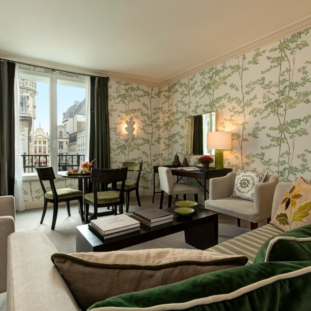Cozy lounge area in the Prestige Suite at hotel amigo in belgium with leaf-patterned wallpaper and green velvet chairs.