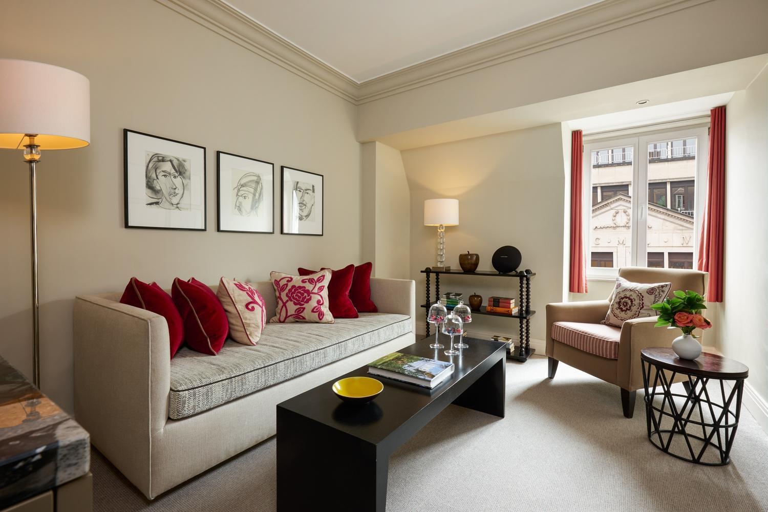 Bright living room at hotel amigo in belgium with a sofa, red pillows, and three framed sketches on the wall.