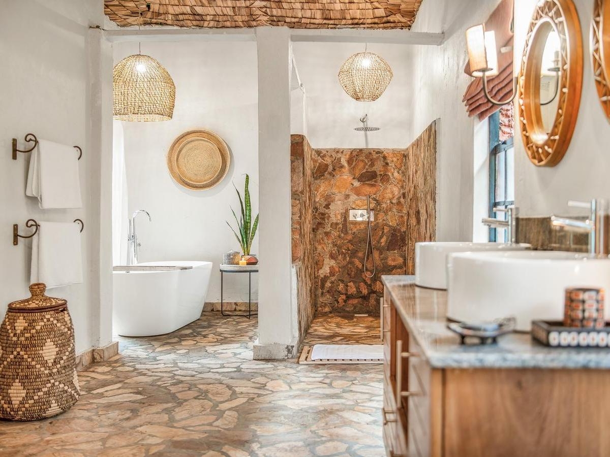 Spacious bathroom at Mahogany Springs uganda with a white freestanding tub, stone shower enclosure, and woven decor.