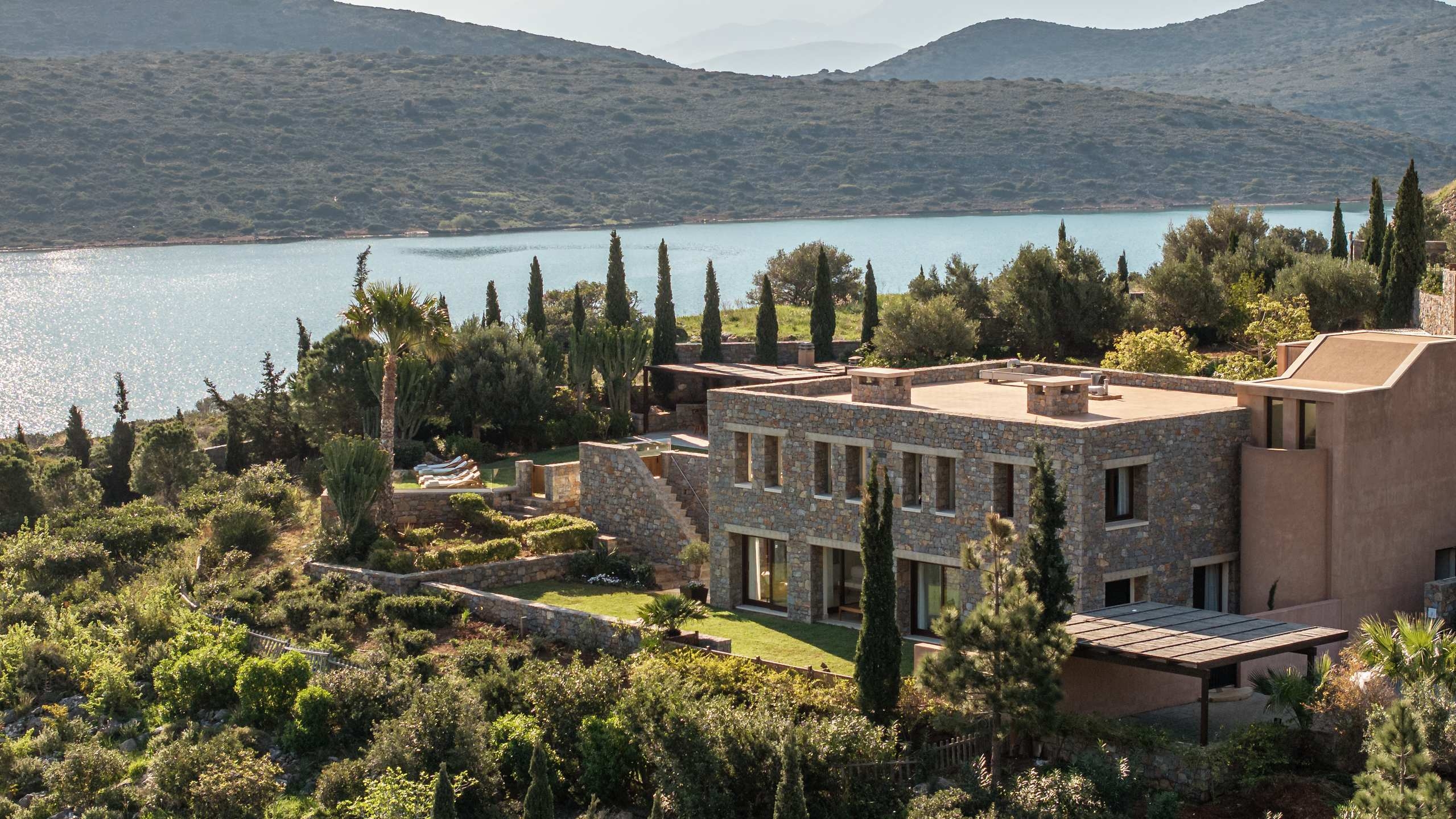 Aerial view of a villa at Phaea Blue Palace in Crete with surrounding trees and water in the background