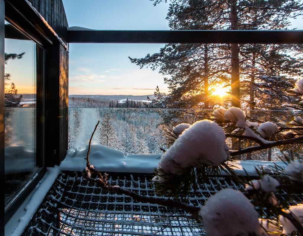 View from a snowy balcony with a net floor looking out over a wintry forest and distant river.