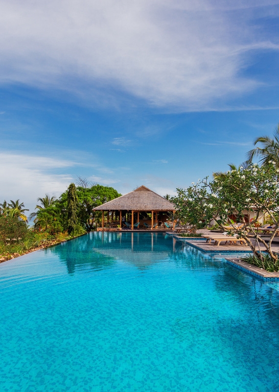 Large infinity swimming pool reflecting a thatched pavilion and palm trees at Zuri Zanzibar resort.