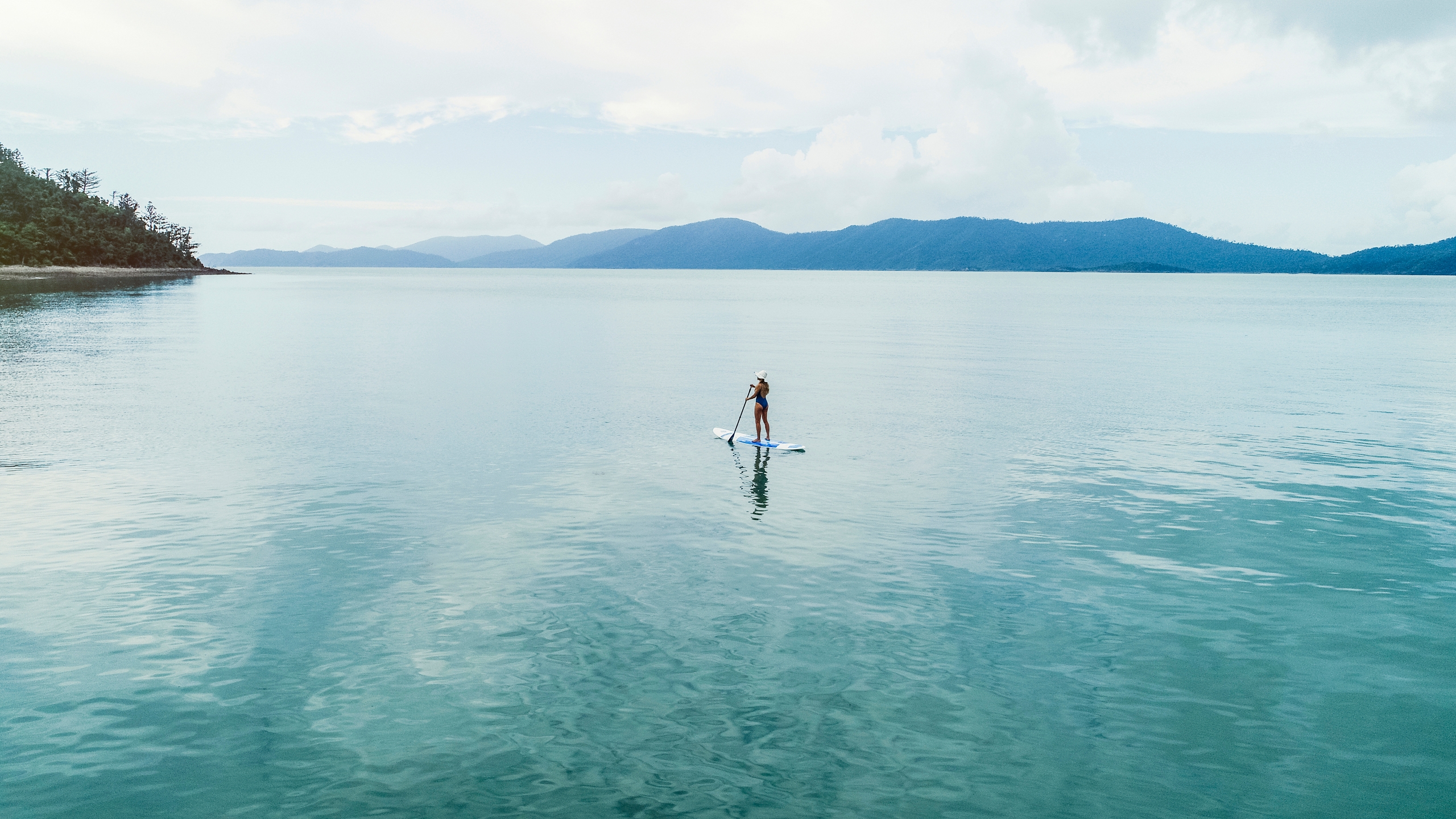 A woman standing on a paddle board paddling through still water