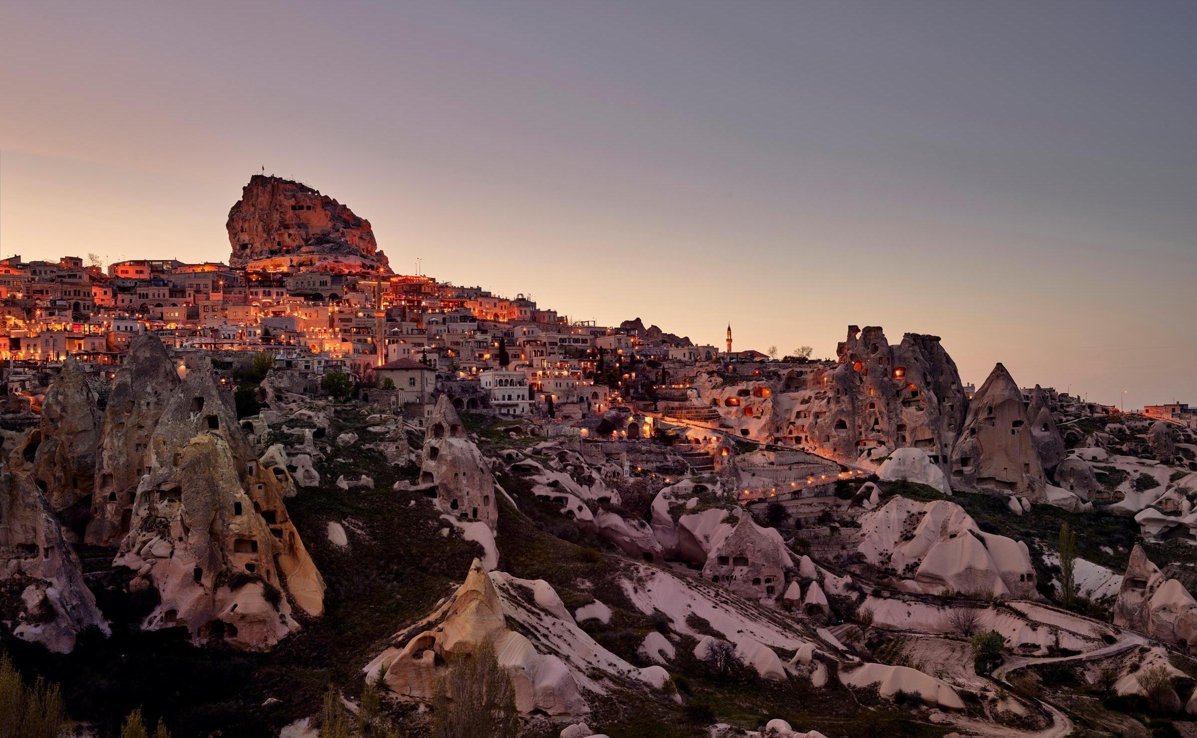 Glowing lights of a hillside town in Cappadocia nestled among ancient rock structures at twilight.