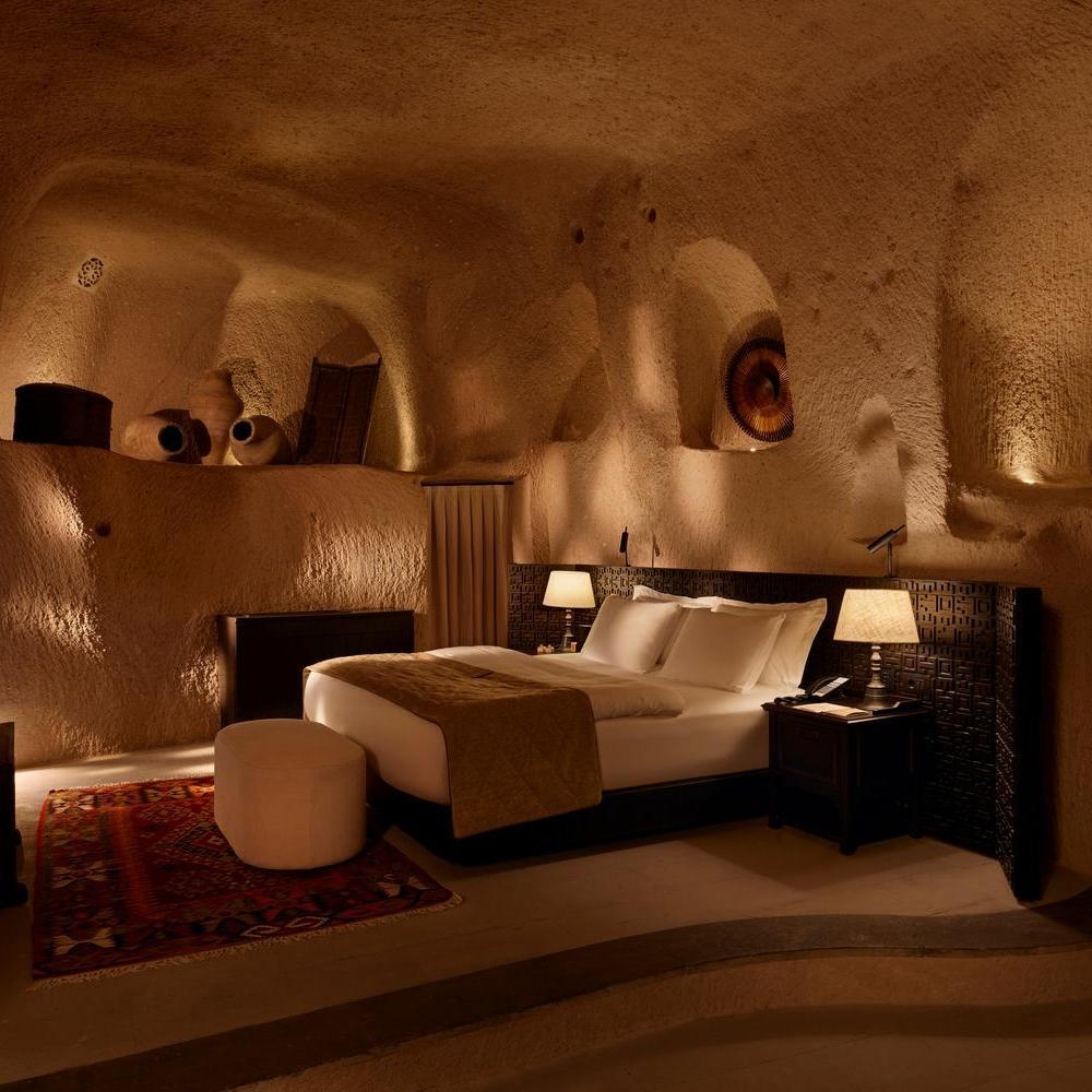 Warmly lit luxury cave hotel room with a large bed, stone walls, and traditional decorative rugs.