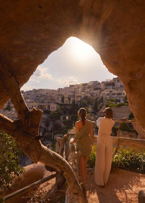 View through a cave opening toward a sunlit village on a hill in Cappadocia.