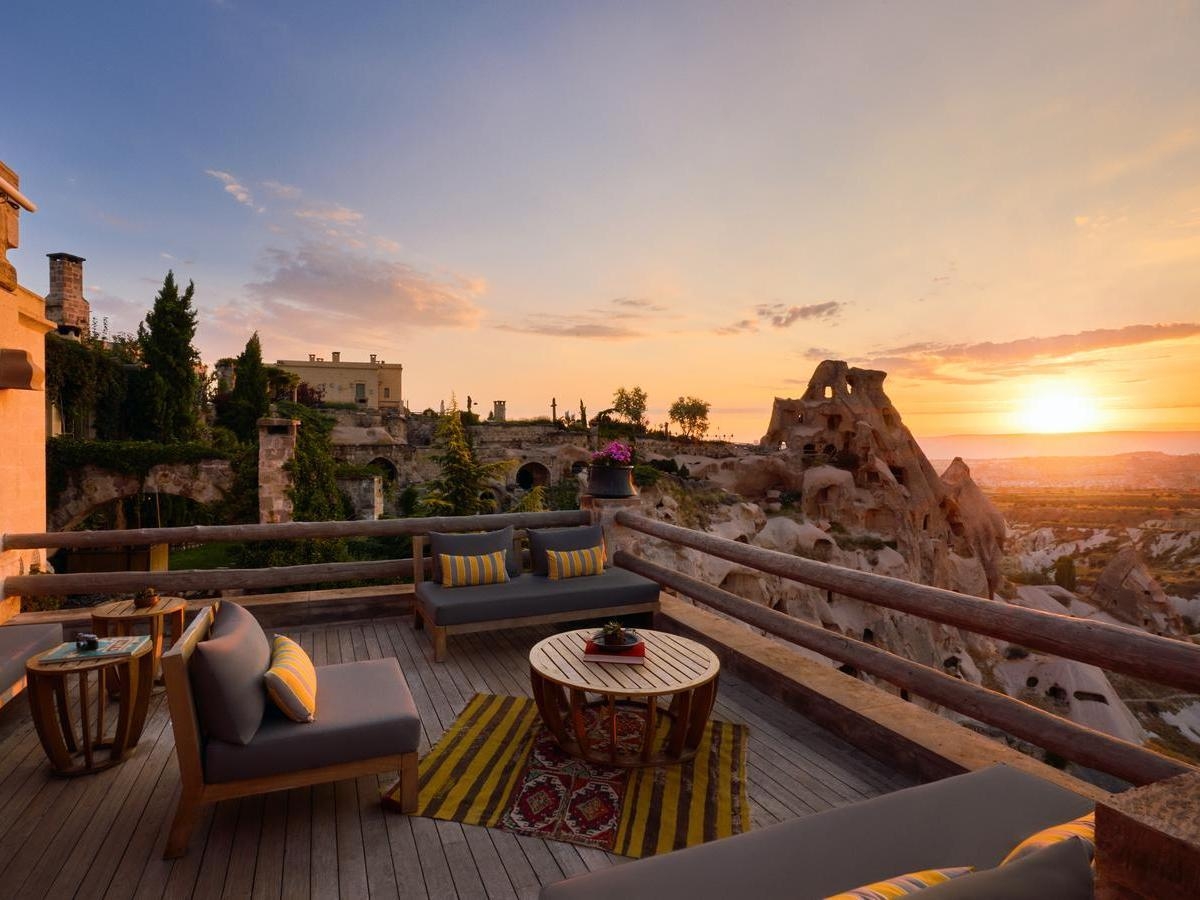 Outdoor lounge area with comfortable seating on a wooden deck overlooking a sunset in Cappadocia.