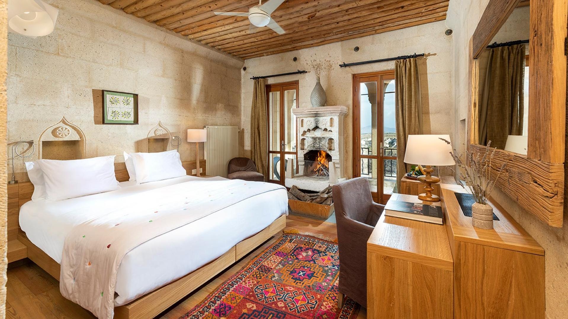 Elegant hotel room with a fireplace, wooden ceiling, and a large bed with white linens.