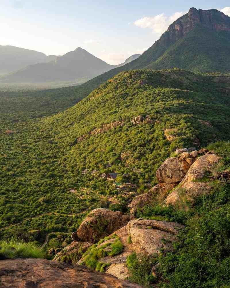 Aerial view of Reteti House on a rocky hill with a pool, overlooking the savanna at sunset under a golden sky.