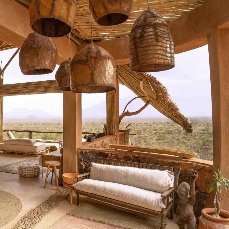 Interior of a lounge with large hanging metal lamps and a white sofa overlooking a savanna landscape.