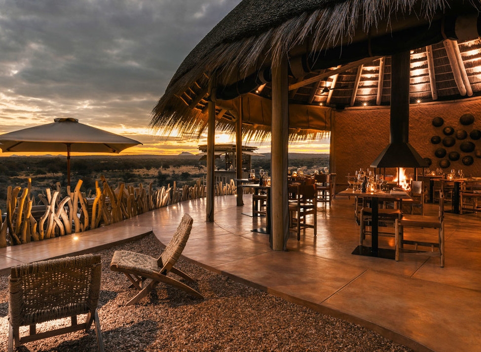 Luxury open-air restaurant at Zannier Hotels Omaanda with thatched roof and tables overlooking a sunset savanna.