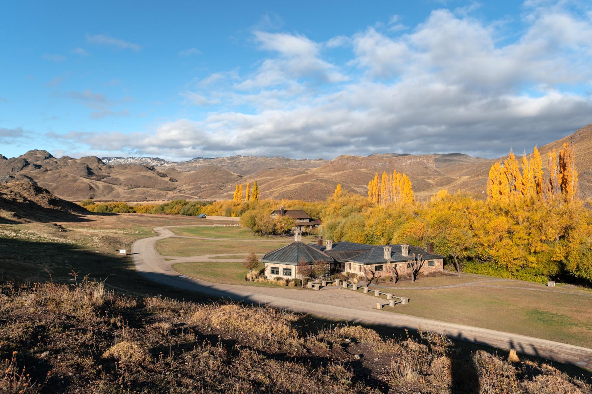 Elevated view of a stone lodge surrounded by golden autumn trees and hills at Explora Patagonia National Park.