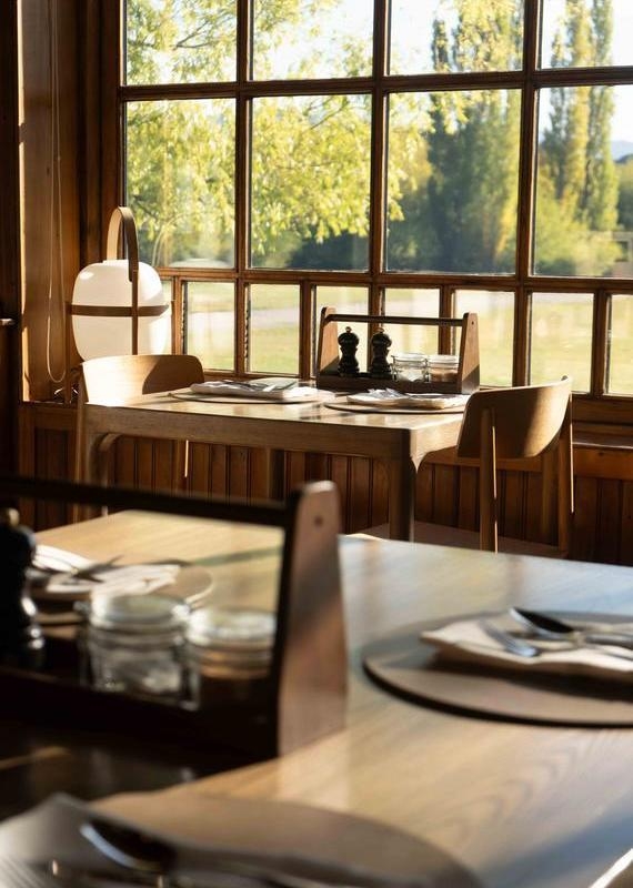 A wooden dining table next to a grid window with a view of autumn trees at Explora Patagonia National Park.