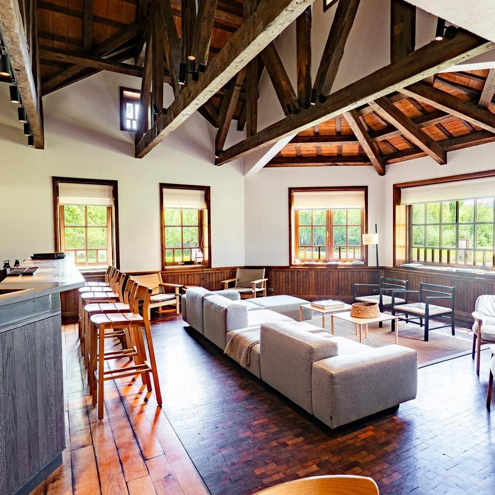 Rustic lodge lounge at Explora Patagonia National Park with exposed wooden beams, gray couches, and large windows.