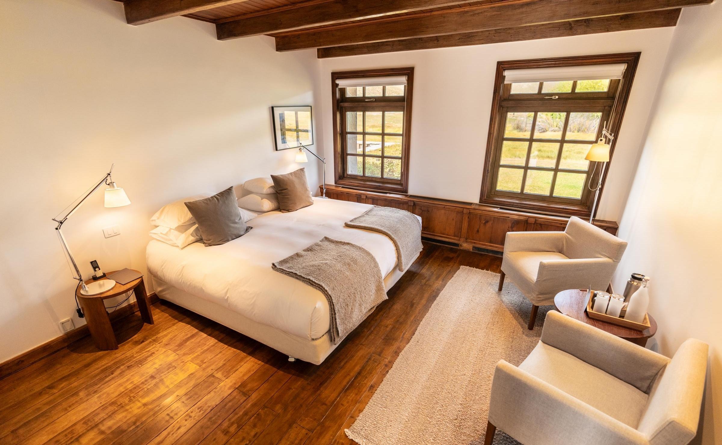 A bright bedroom with a large bed, wooden floors, and armchairs at Explora Patagonia National Park.