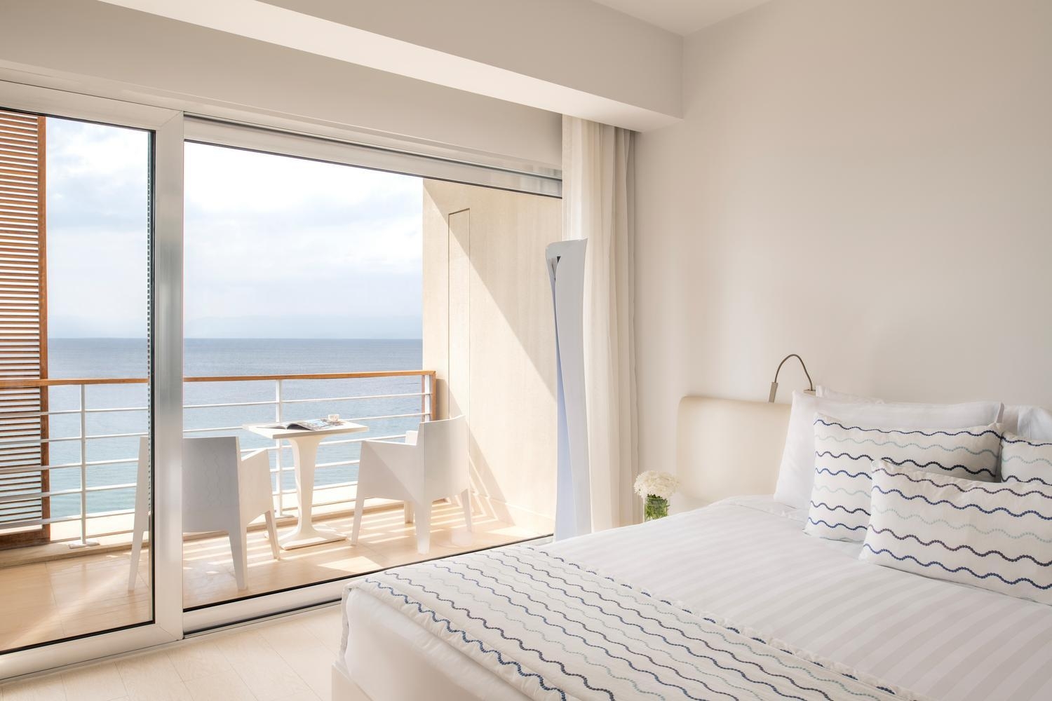 Bright white hotel room at Kempinski Hotel Aqaba with sliding glass doors opening to a balcony overlooking the sea.