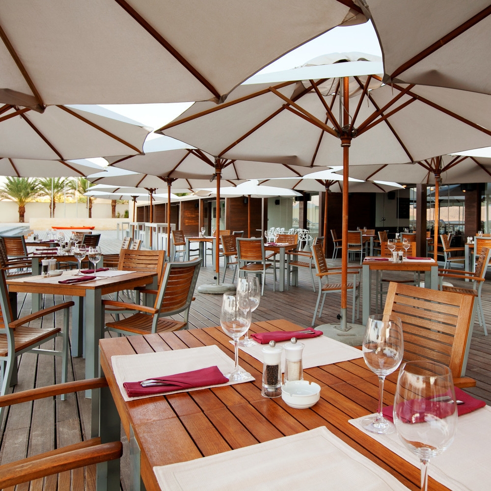 Outdoor wooden dining deck at Kempinski Hotel Aqaba shaded by white umbrellas, with tables set for a meal.