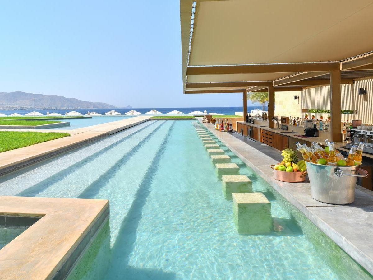 Swim-up pool bar at Kempinski Hotel Aqaba with underwater seating blocks and a counter holding drinks in ice buckets.