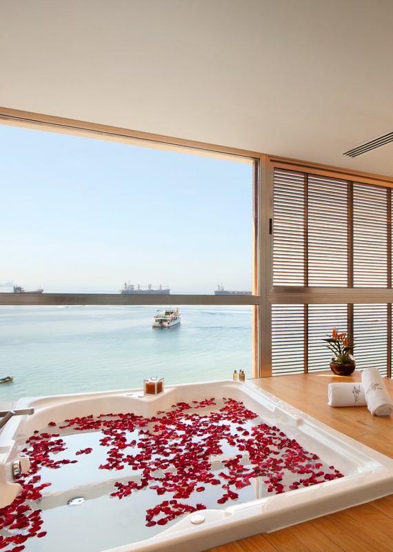 Indoor jacuzzi filled with red rose petals at Kempinski Hotel Aqaba, situated next to large windows overlooking the sea.