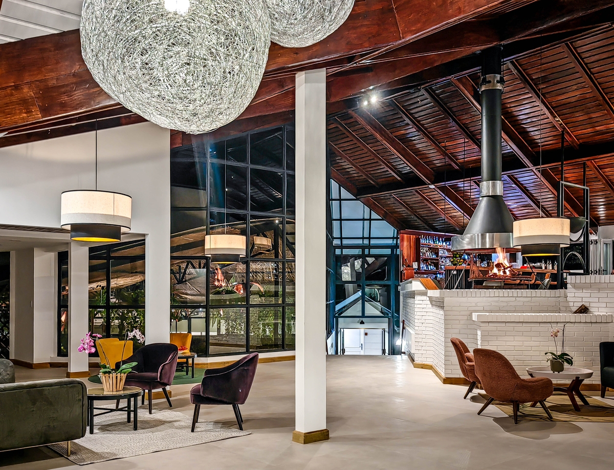 A spacious indoor lounge with a white brick fireplace, vaulted wood ceiling, and stylish armchairs.