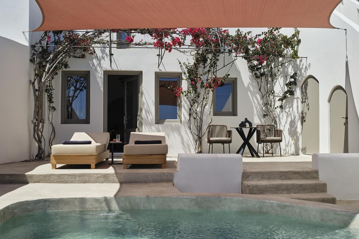 Private pool area at Andronis luxury suites with two sun loungers, white walls with pink bougainvillea, and a shade sail.
