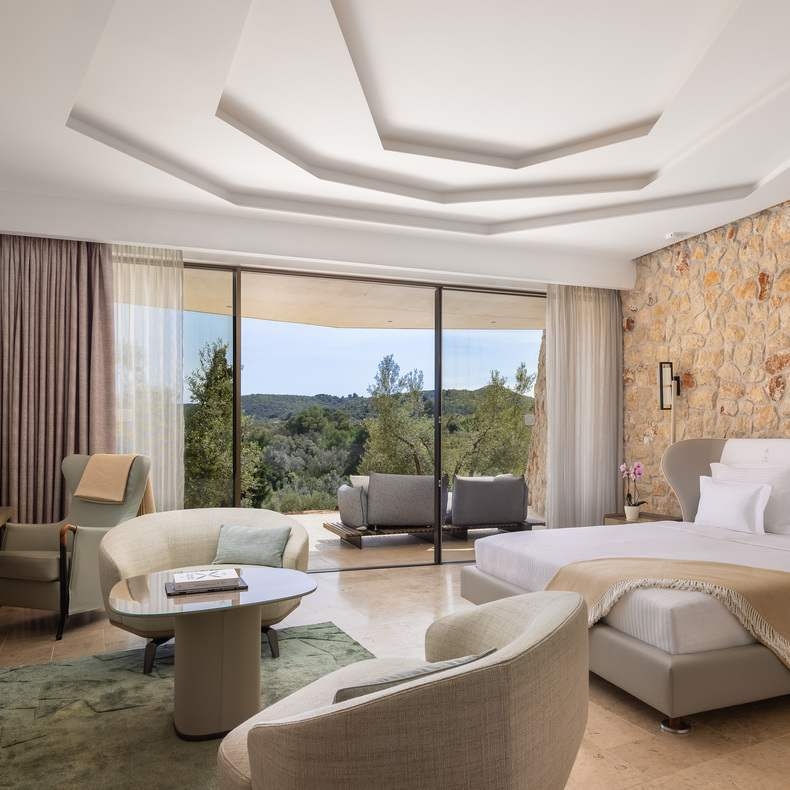 A stylishly designed hotel room with a large bed, seating area, and glass doors showcasing nature views.