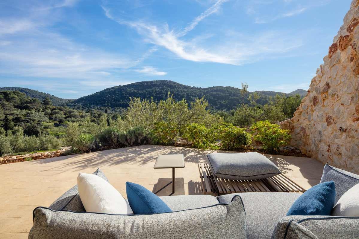 An outdoor stone terrace with comfortable grey and blue seating looking out over green hills and trees.