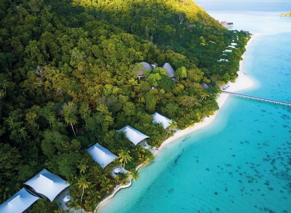 Aerial view of luxury beach suites on a tropical island with turquoise water and dense forest at Bawah Reserve.