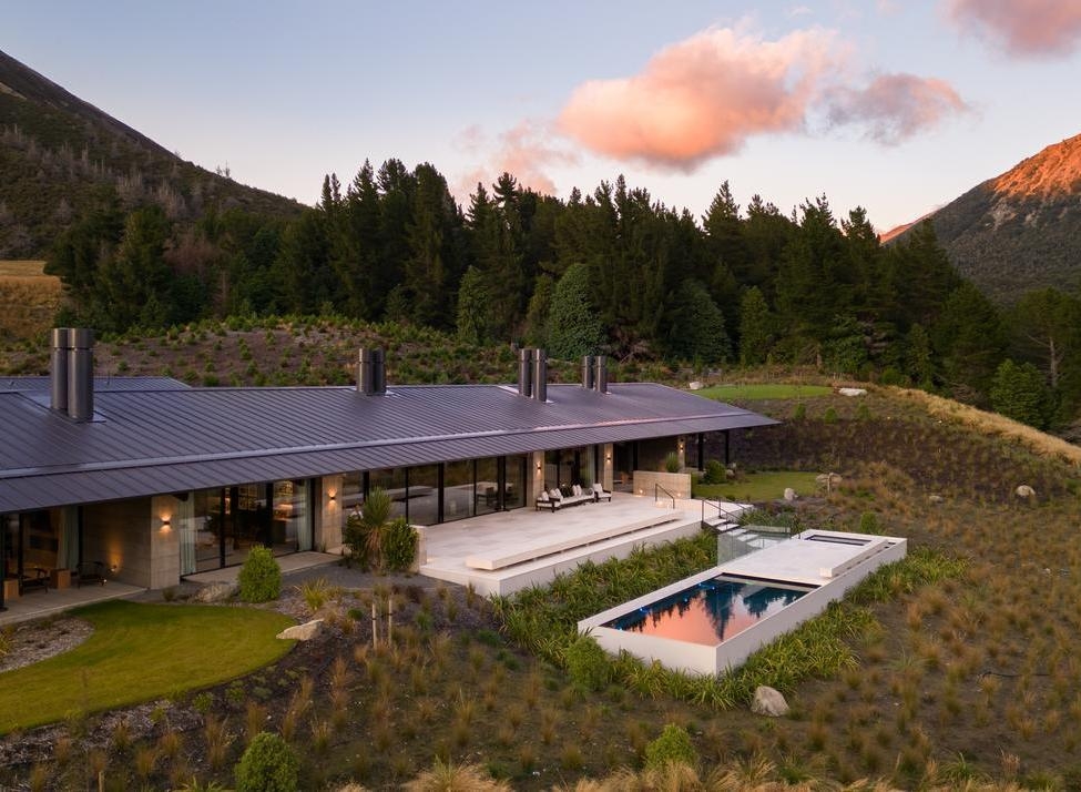 Aerial view of the Homestead at Flockhill Lodge, with a swimming pool, patio, and forest surrounded by mountains at sunset.