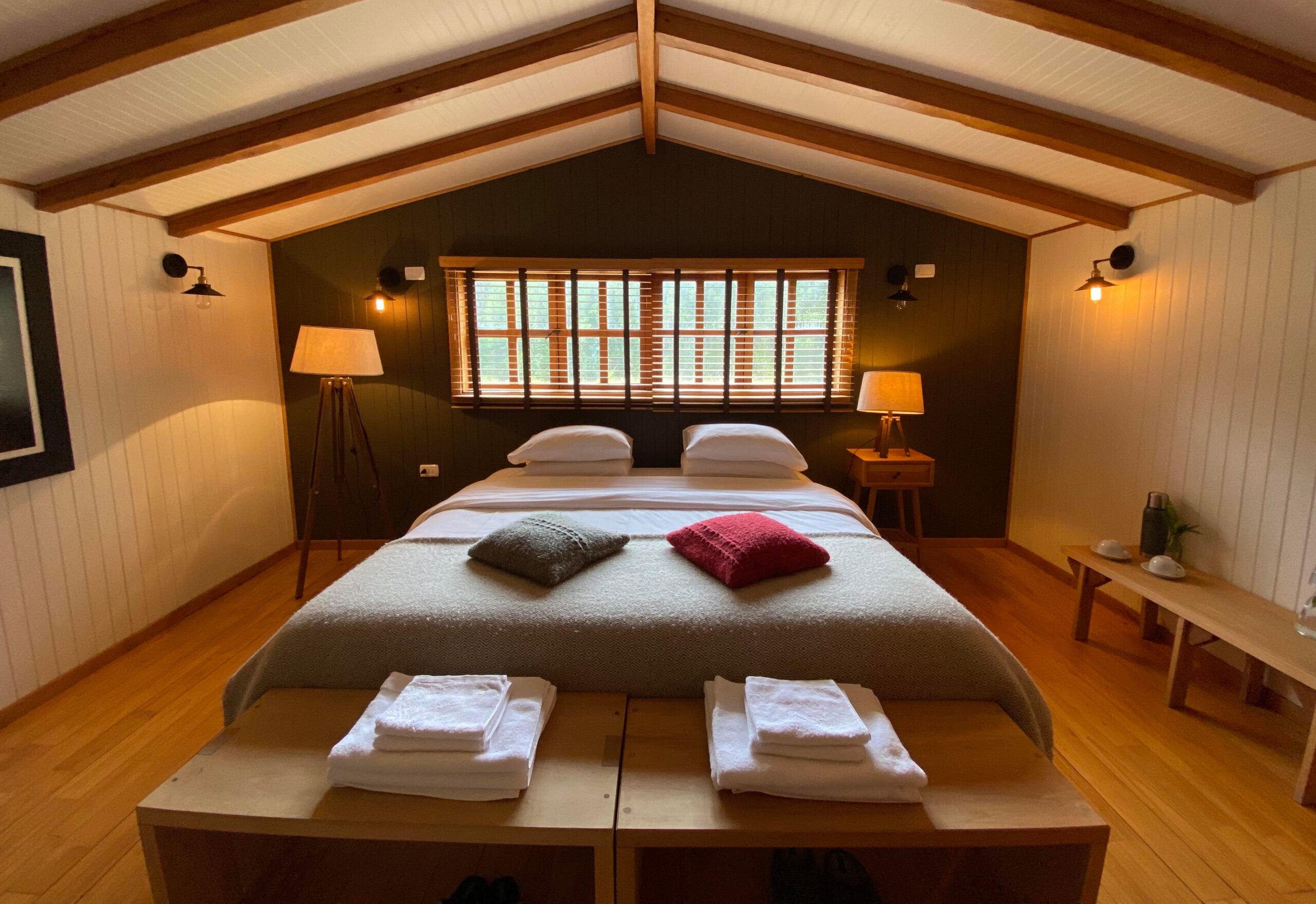Cozy bedroom with a large bed, wooden accents, warm lighting, and two windows.