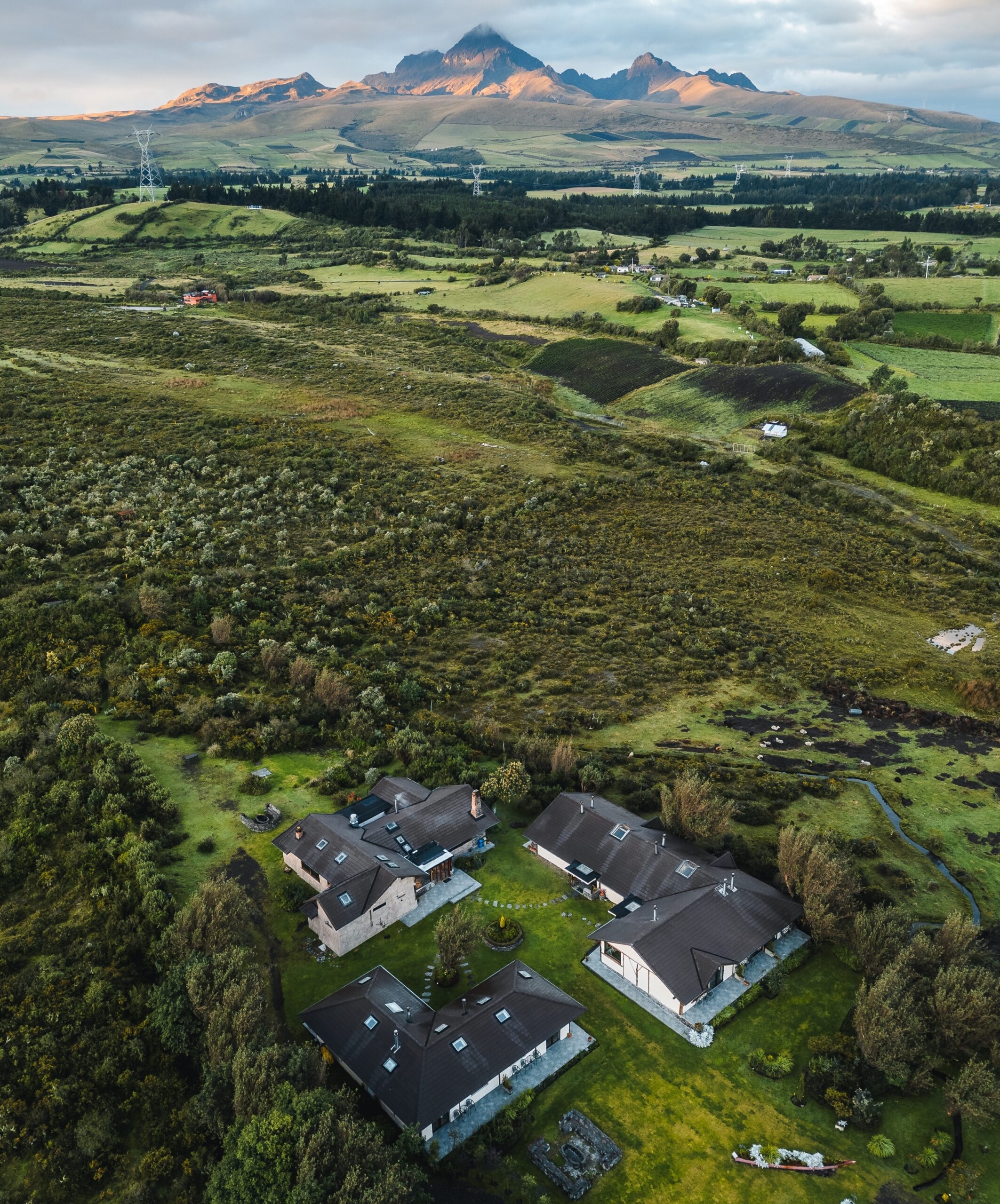 Aerial view of rural landscape with houses, green fields, and distant mountains at sunrise.