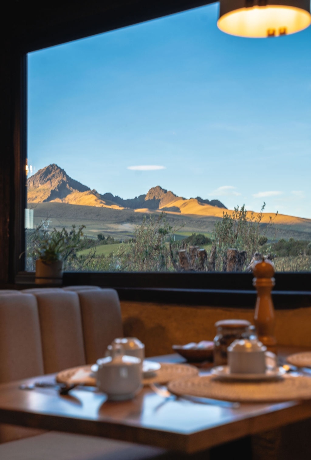 Dining table with a view of mountains through a large window at dusk.