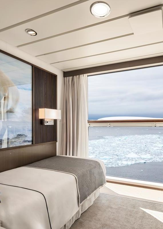 Single bed in a ship cabin with a large window viewing icy water and a polar bear artwork on the wall.