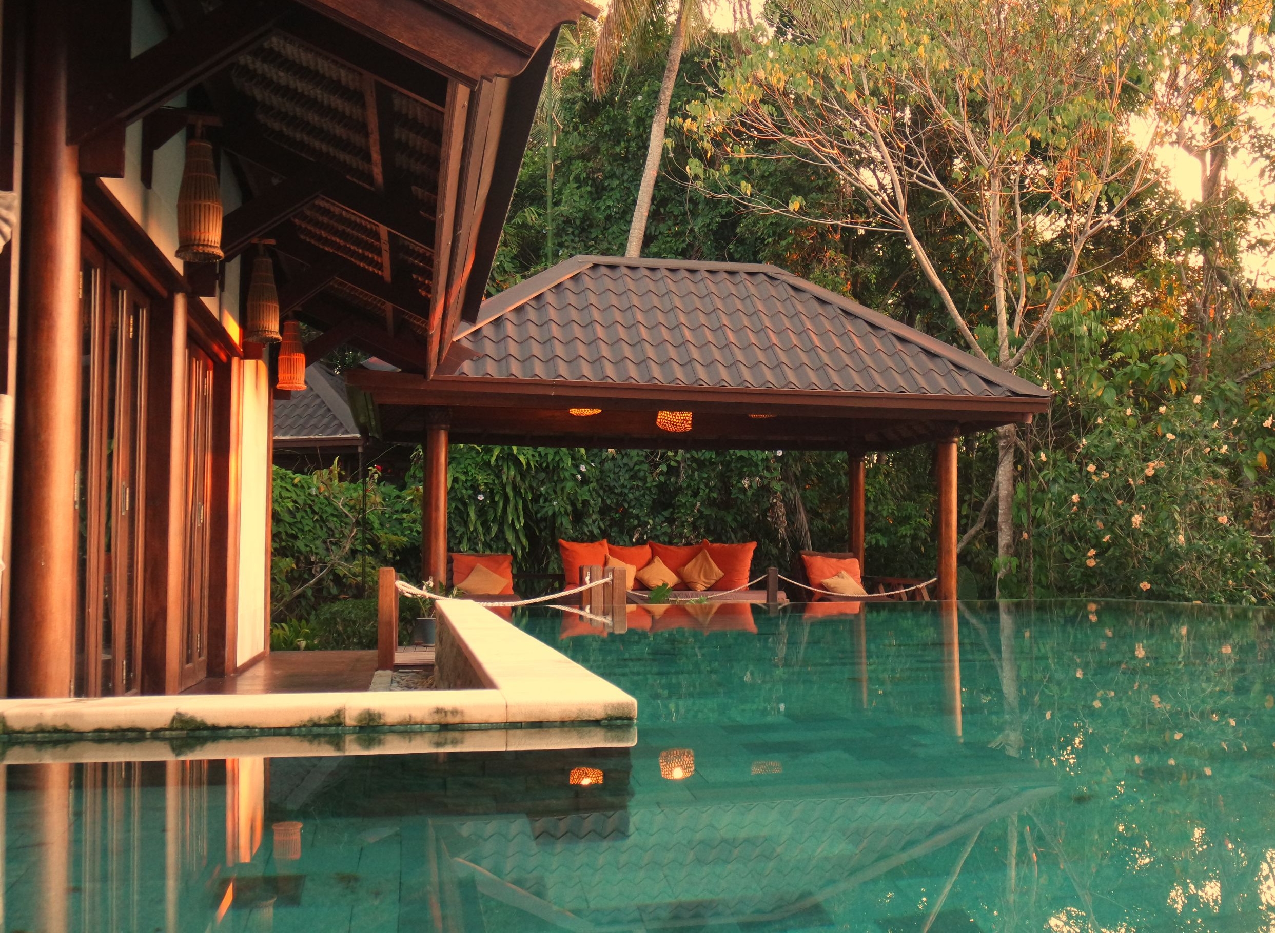 Exterior of a pool with covered lounge area and trees in the background.