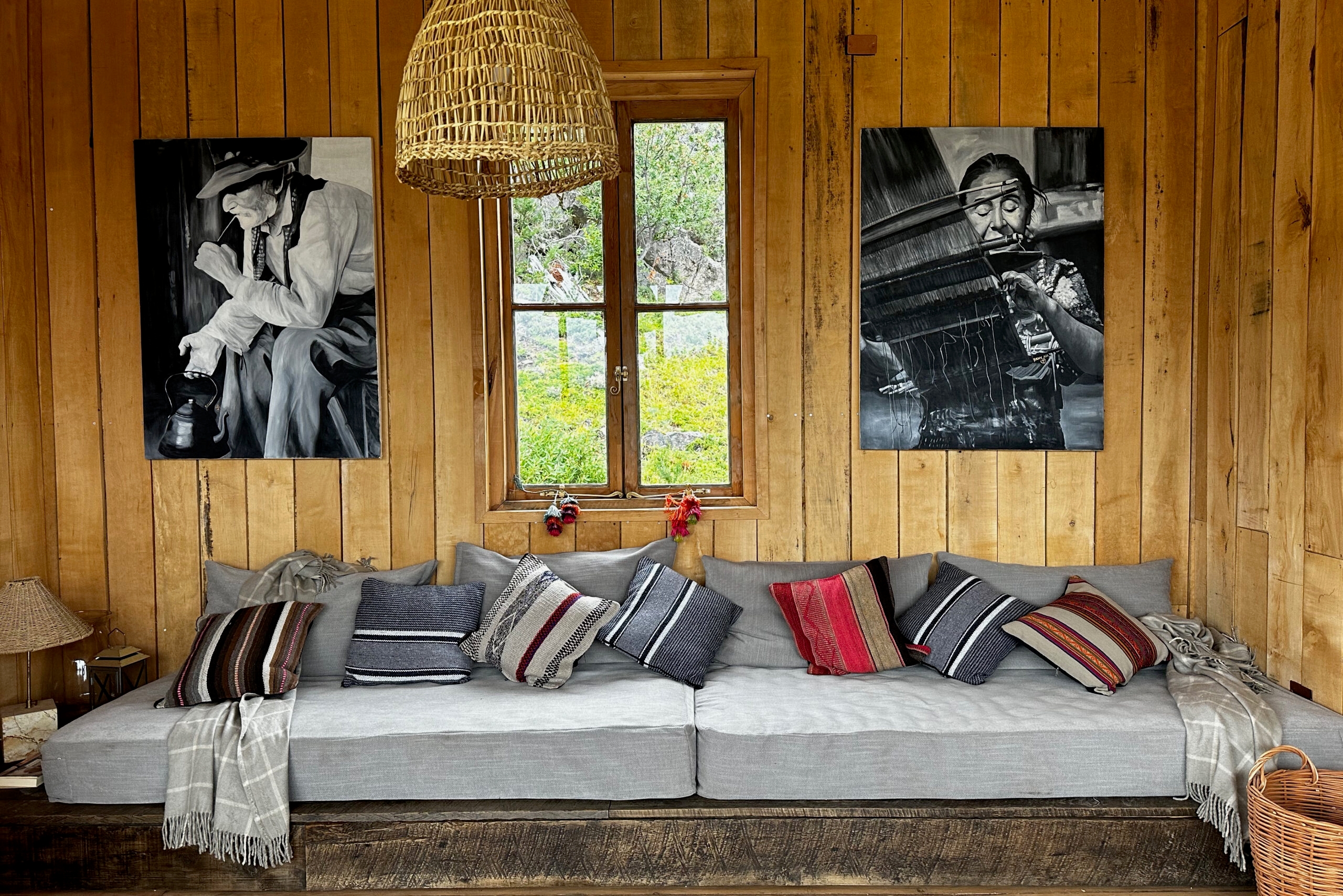 Wood-panelled wall with two large black-and-white portrait photographs above a long, cushioned sofa decorated with striped and textured pillows.