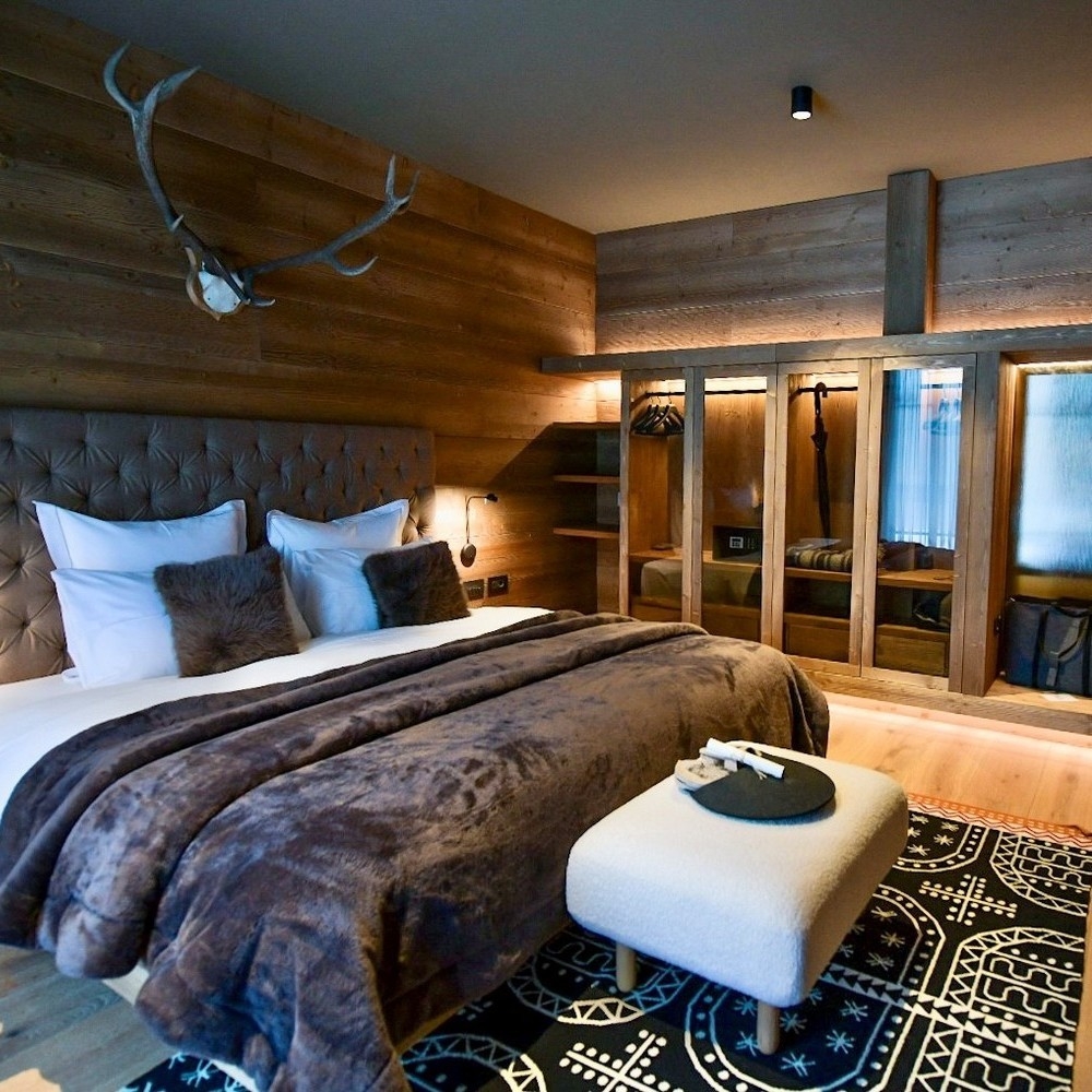 Cozy bedroom with a large bed, brown fur pillows, wood-paneled walls, and a glass-door wardrobe.
