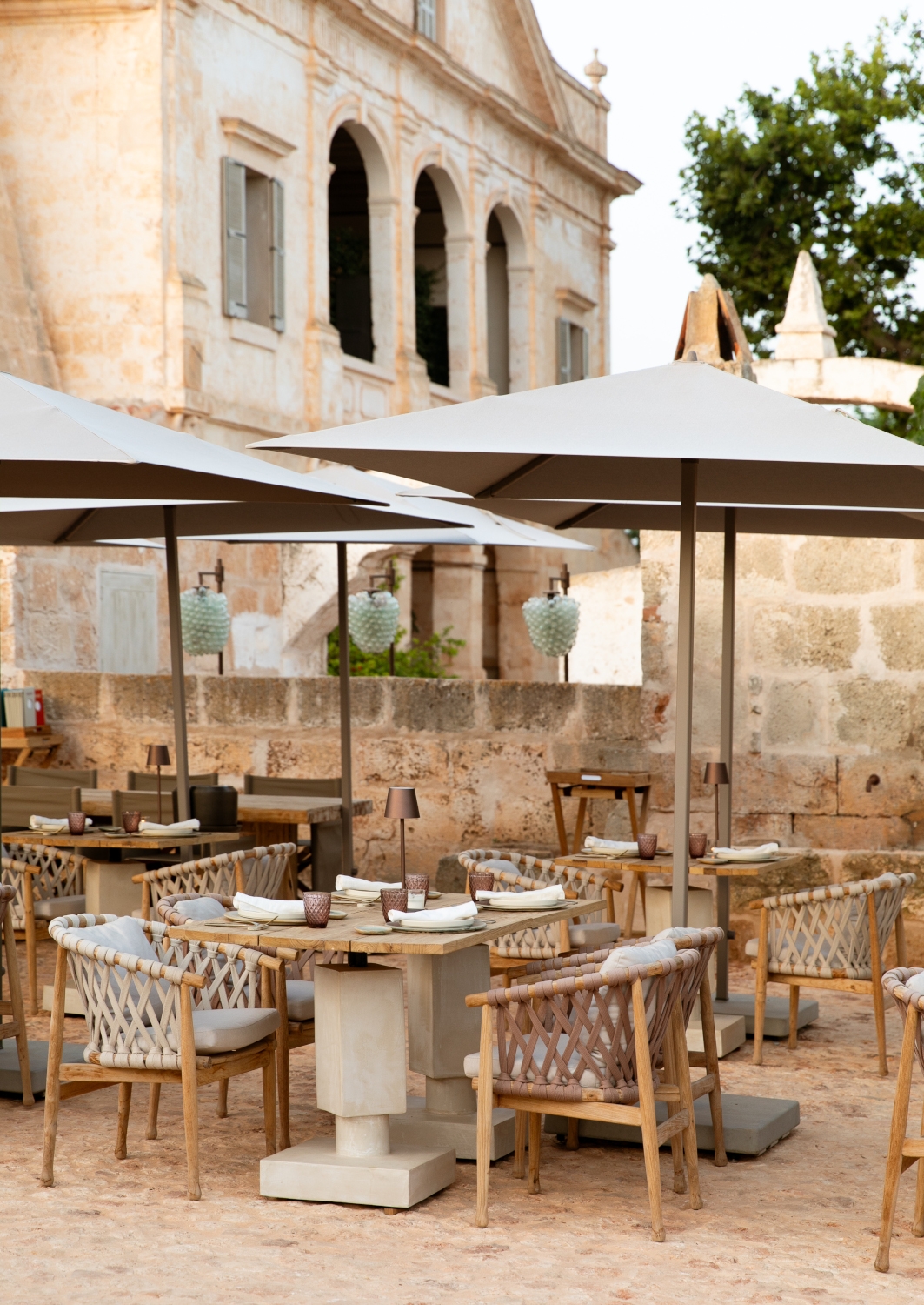 Outdoor dining tables with parasols at Son Vell in Balearic Islands Spain set against a historic stone facade.