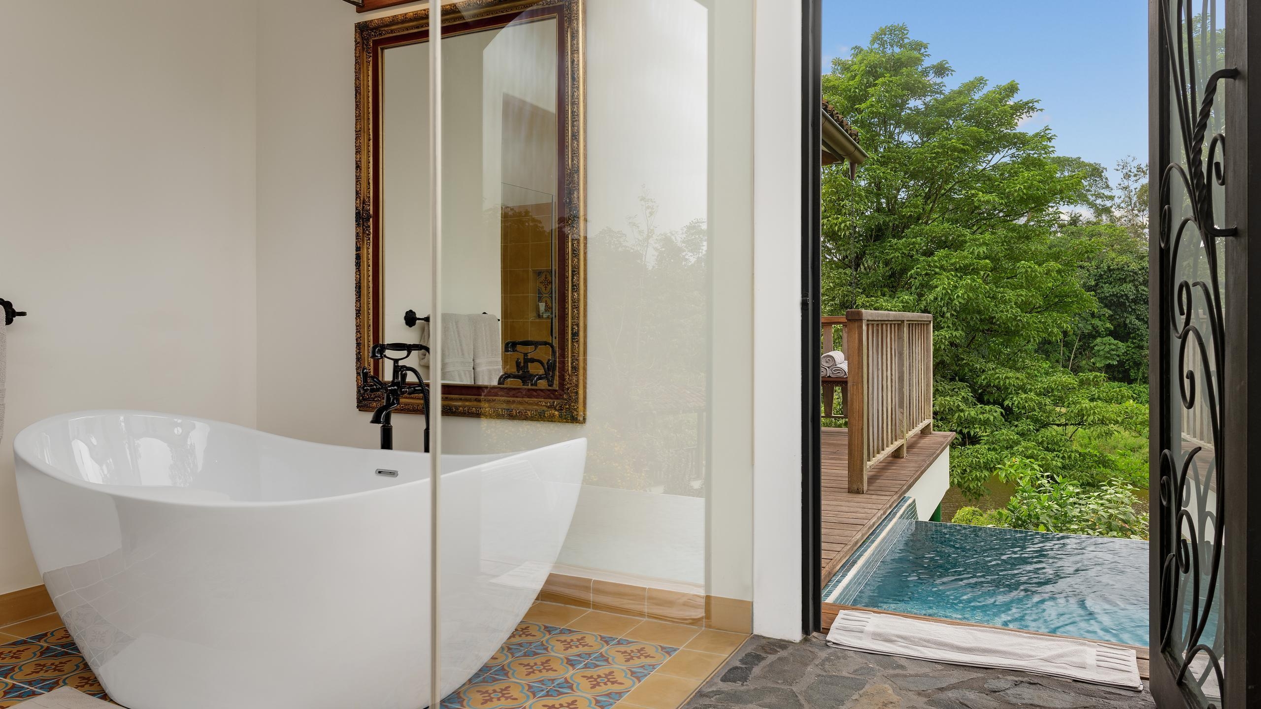A white freestanding bathtub in a room with patterned tiles and a door opening to a private outdoor pool.