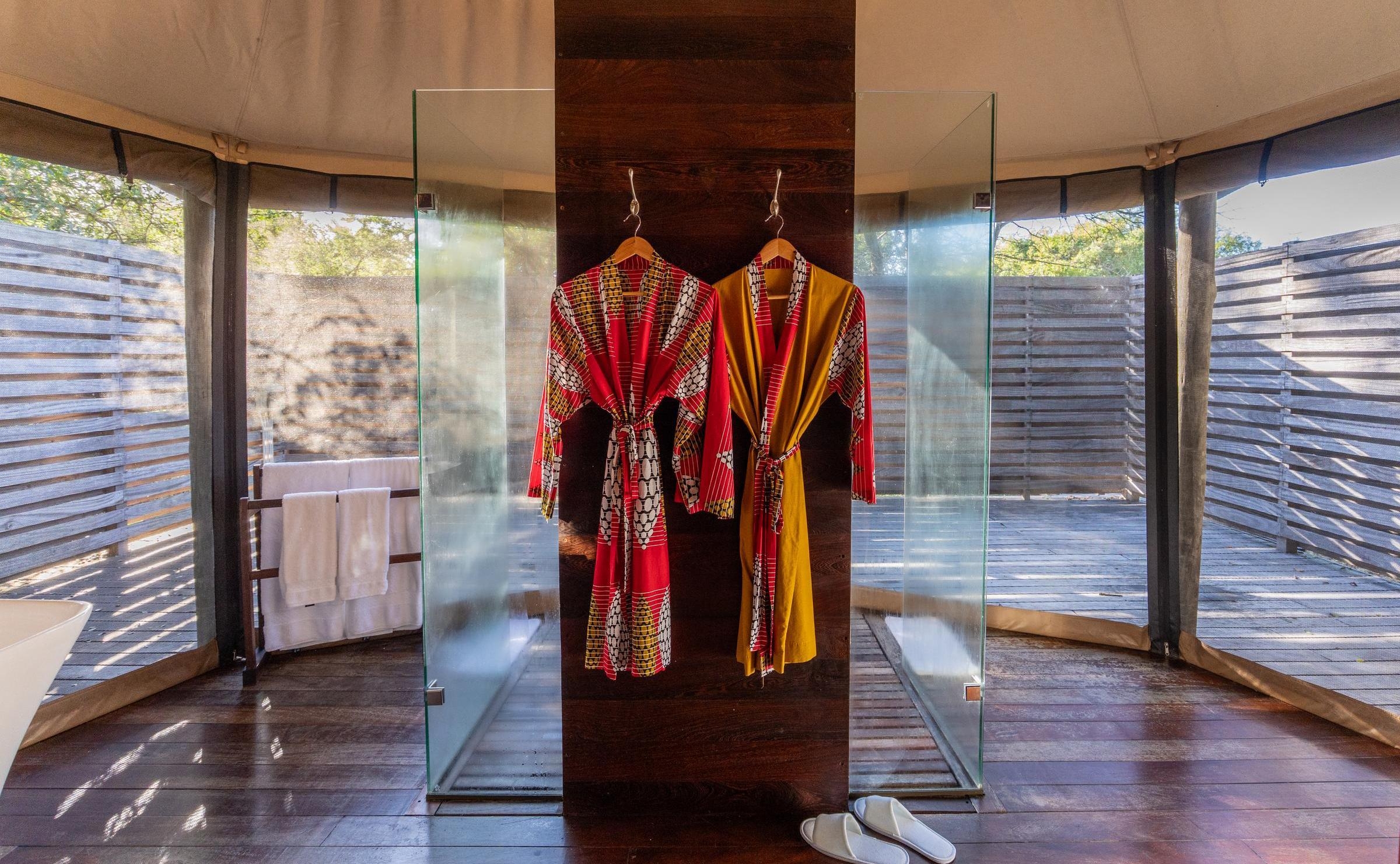 Red and yellow patterned robes hang on a wooden partition between two glass showers in a luxury tented suite.