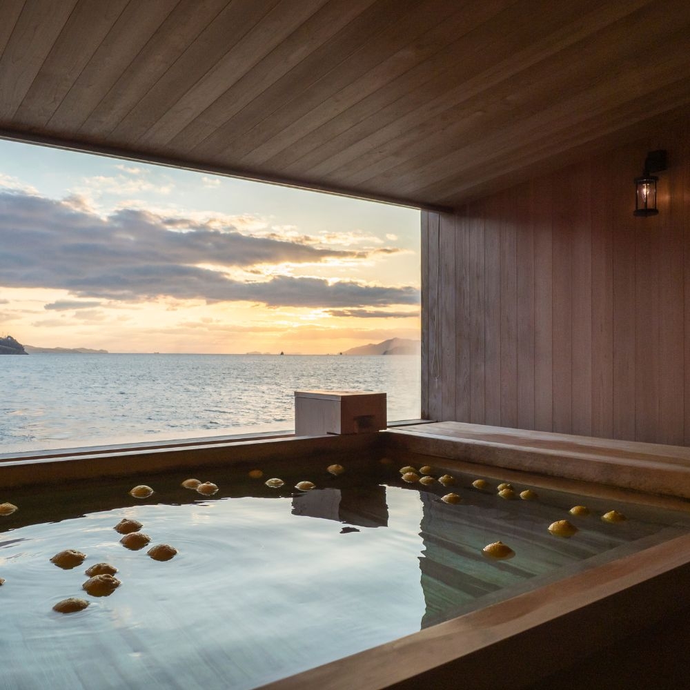 A large bath with lemons floating in it and a sunset sea view behind it